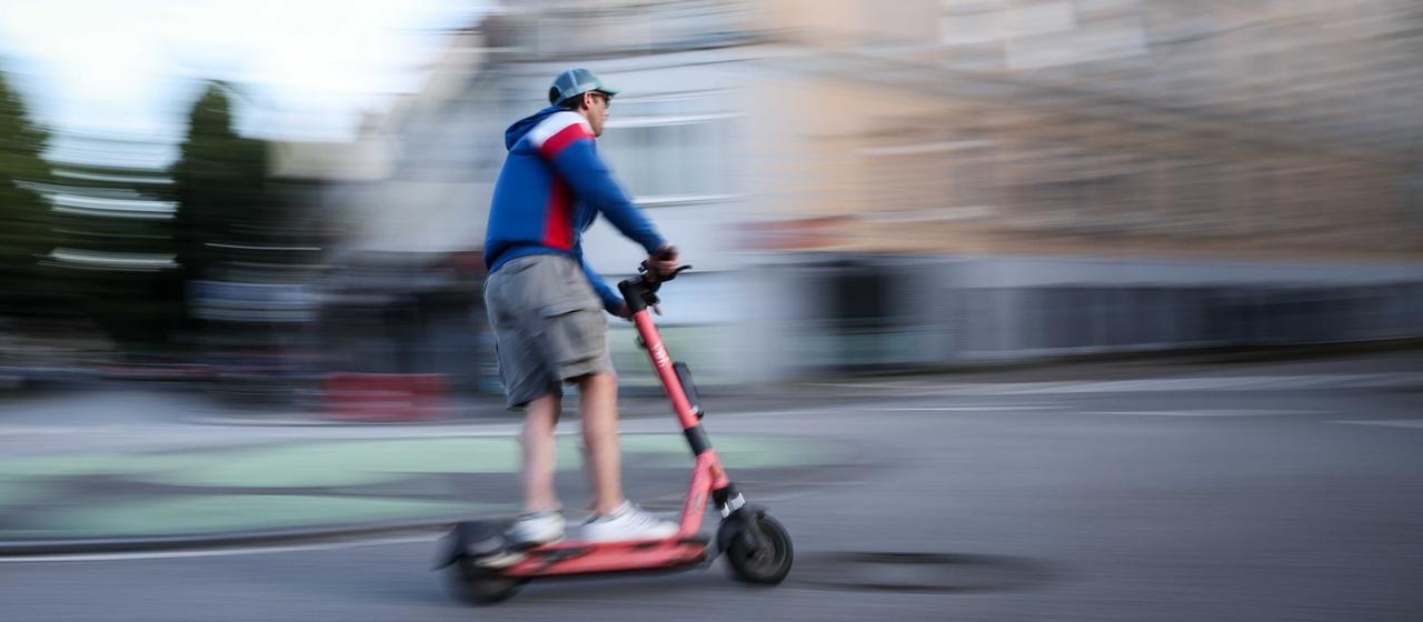 Ein Mann fährt auf einem roten e-Scooter eine Straße entlang
