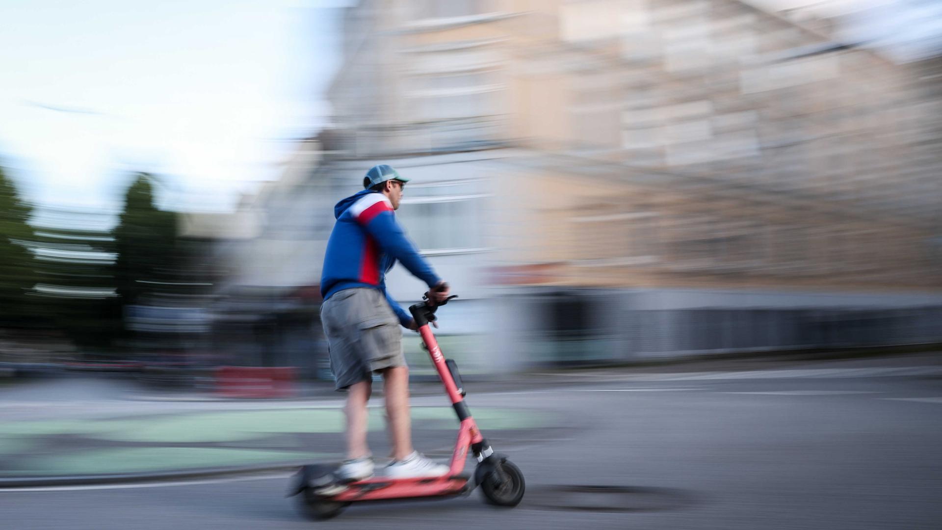 Ein Mann fährt auf einem roten e-Scooter eine Straße entlang | dpa