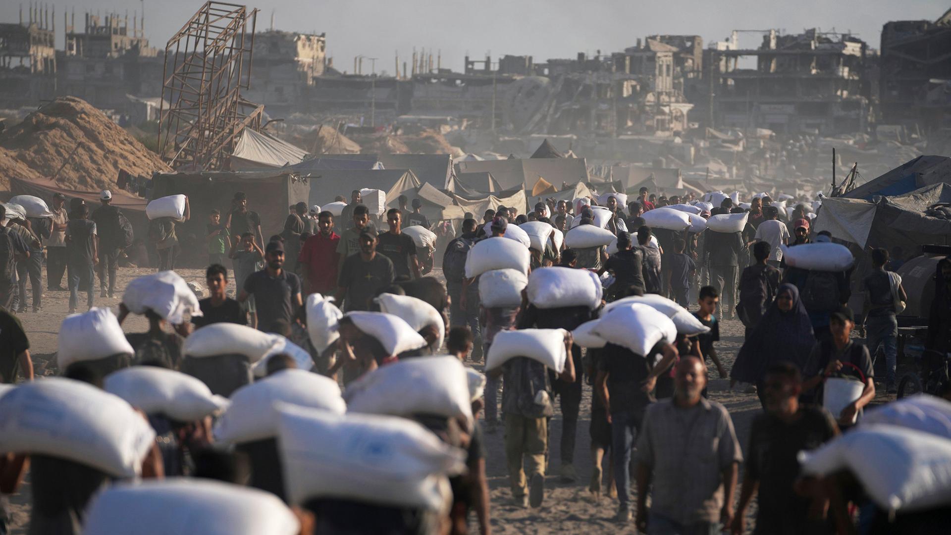 Menschen tragen Säcke, die von einem humanitären Hilfskonvoi abgeladen wurden. | AP