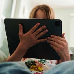 Eine Jugendliche sitzt mit einem Tablet auf einem Sofa