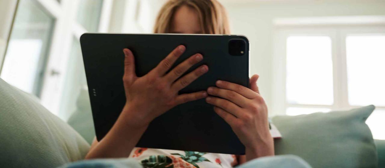 Eine Jugendliche sitzt mit einem Tablet auf einem Sofa.