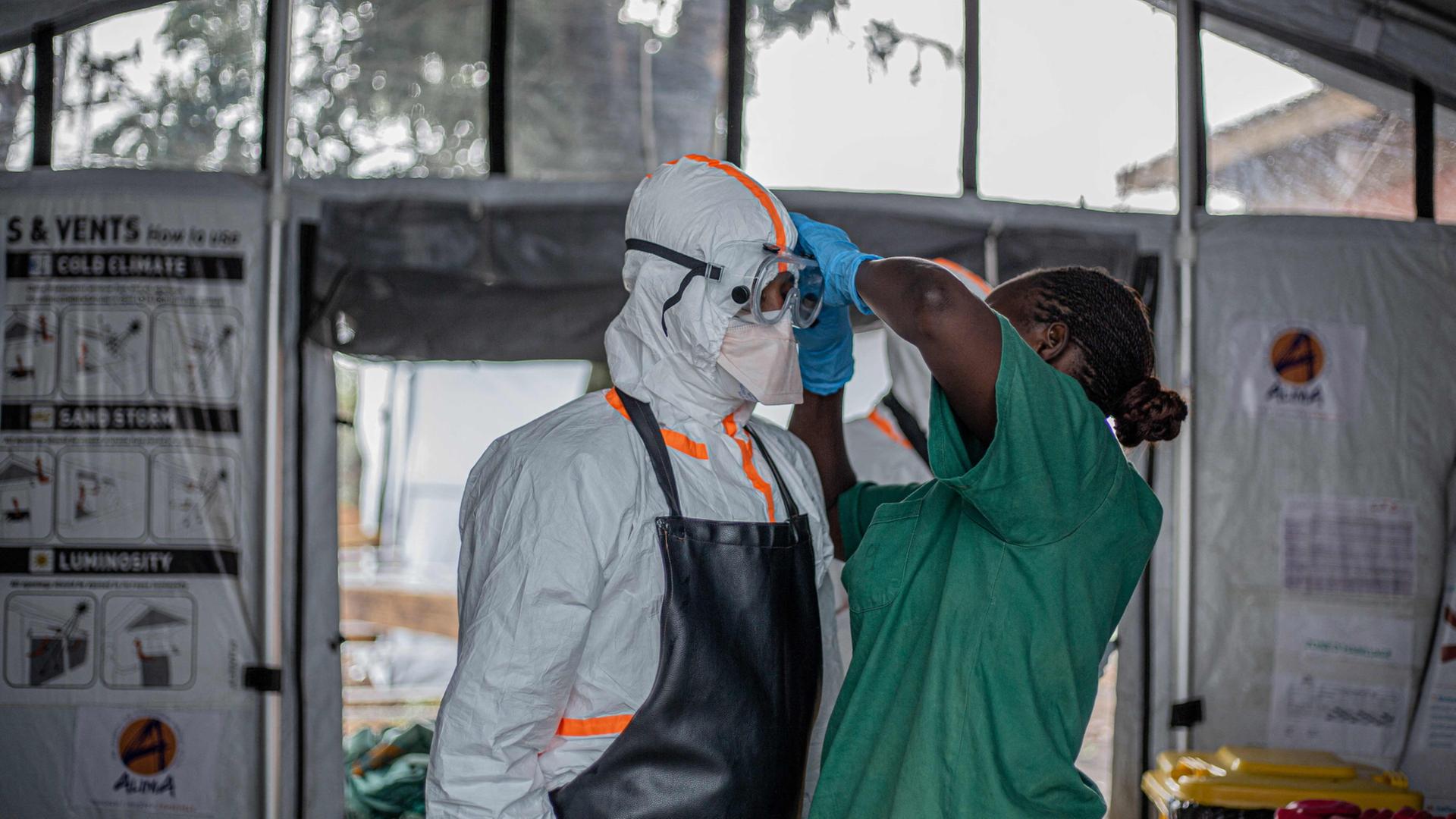 Ein Hygienehelfer hilft einem Arzt, persönliche Schutzausrüstung (PSA) anzuziehen, bevor er das Rwampara Ebola Treatment Centre (ETC) betritt, | AFP