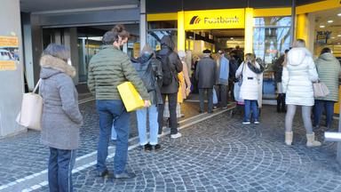 Kunden stehen Schlange vor einer Postbankfiliale.