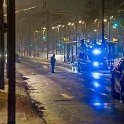 Polizeiwagen mit eingeschaltetem Blaulicht auf schneeregennasser Straße, Polizisten stehen am Rand, ein Mann hält eine Taschenlampe und leuchtet auf den Boden, im Vordergrund ein schwarzes Auto mit offener, beschädigter Motorhaube
