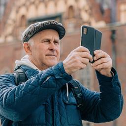 Ein älterer Mann macht in Breslau ein Foto mit seinem Smartphone.