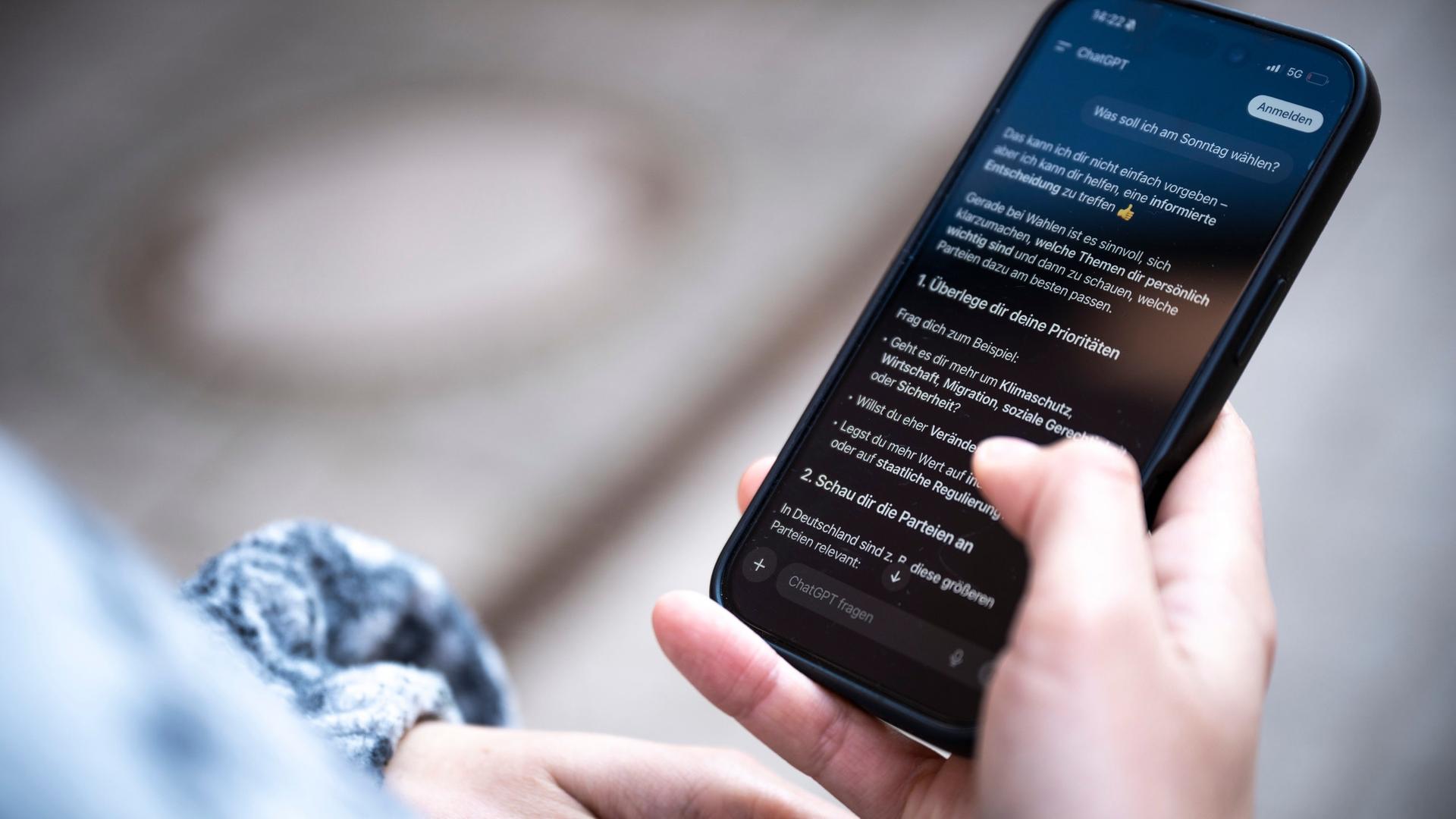 Eine Person hält ein Smartphone in der Hand und liest in der Anwendung ChatGPT eine Antwort auf die Frage 