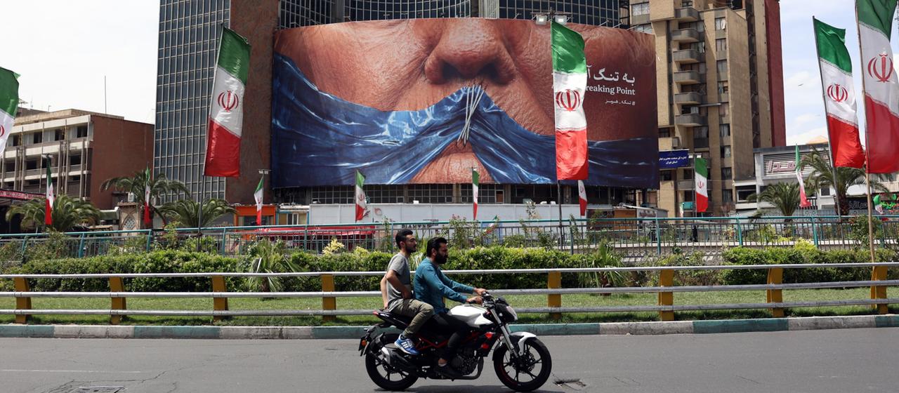 Menschen fahren auf dem Valiasr-Platz in Teheran, Iran, an einer riesigen Anti-US-Plakatwand mit einem Foto von US-Präsident Donald Trump vorbei. 