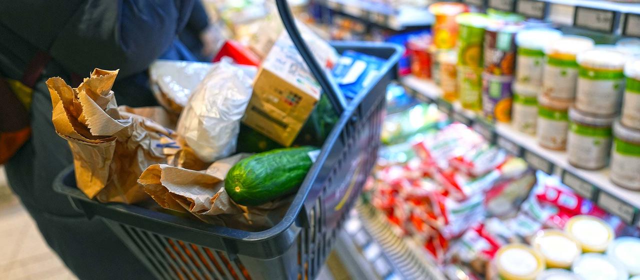 Eine Kundin mit Einkaufskorb geht an den Regalen in einem Supermarkt vorbei.