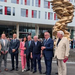 Mehrere Männer und eine Frau machen ein Gruppenfoto vor einer goldenen Skulptur.