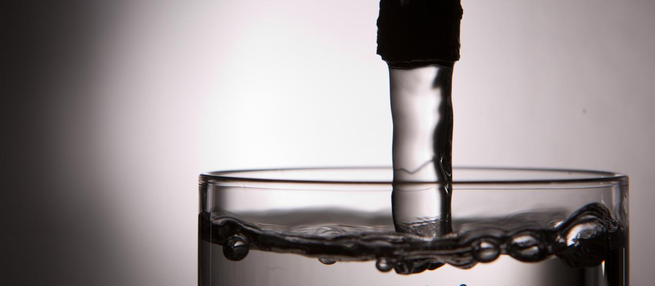 Wasser fließt aus einem Hahn in ein Glas.