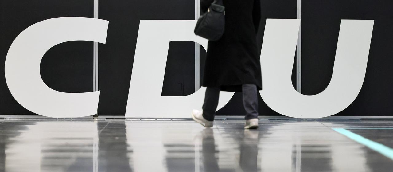Eine Person in Mantel läuft an einem CDU-Logo vorbei.