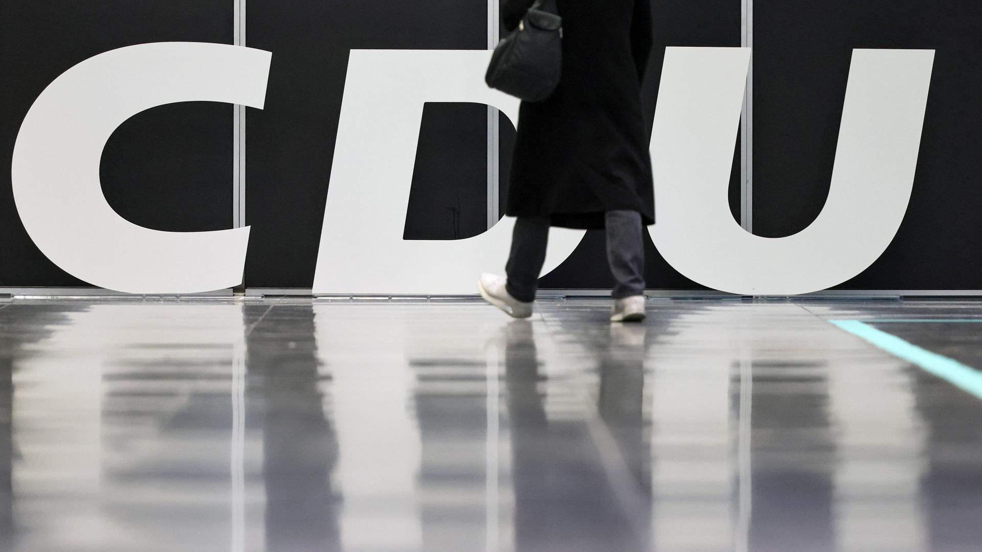 Eine Person in Mantel läuft an einem CDU-Logo vorbei. | EPA