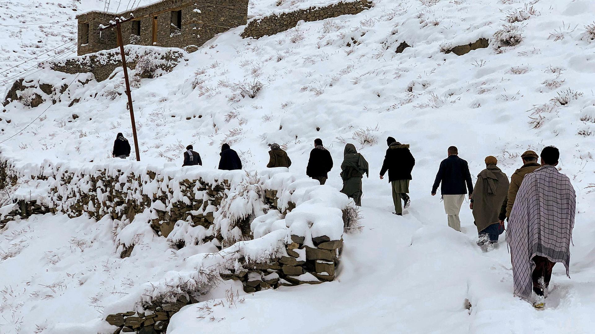 Mehrere Personen laufen auf einem verschneiten Pfad an einer Steinmauer und einem Haus entlang einen HÃ¼gel hinauf. | AFP