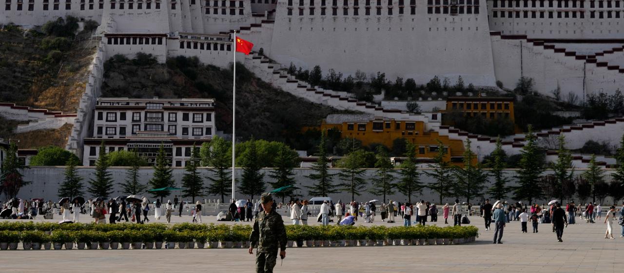 Ein Soldat läuft auf einem öffentlichen Platz im Westen Tibets, im Hintergrund die chinesische Flagge.