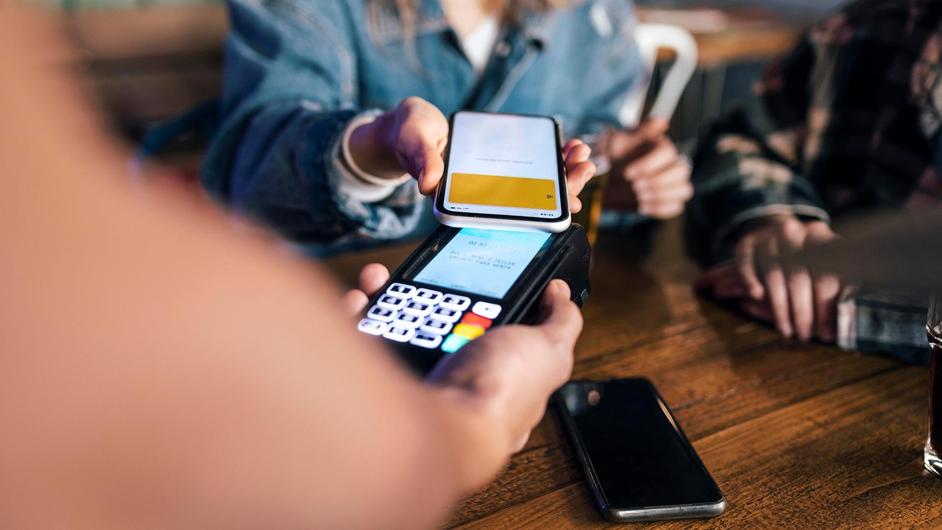 Eine Frau bezahlt in einem Restaurant ihre Rechnung mit ihrem Smartphone. | picture alliance / Westend61