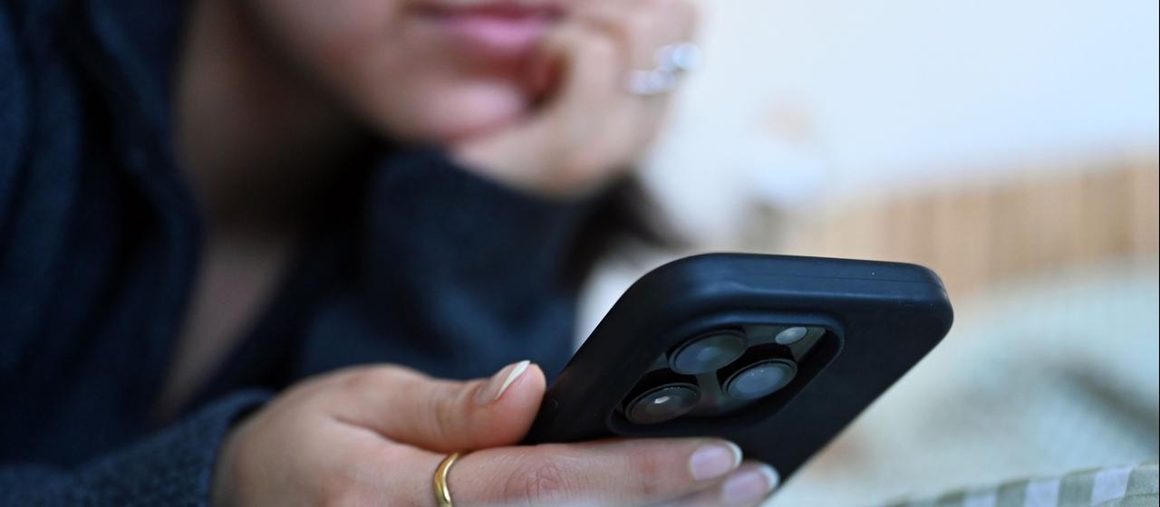 Eine junge Frau liegt mit dem Smartphone in der Hand auf dem Bett.