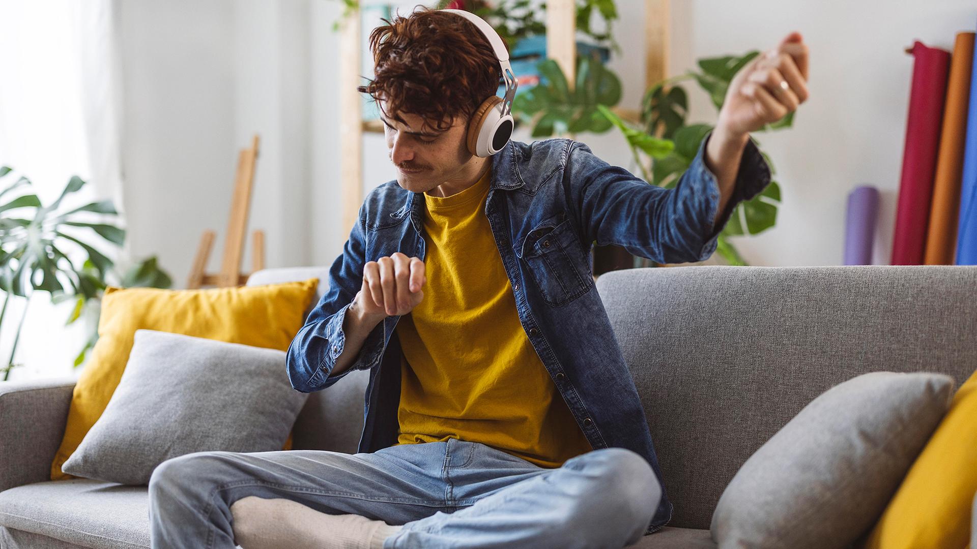 Ein junger Mann hört Musik mit Kopfhörern. | picture alliance / Westend61