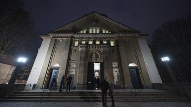 Menschen stehen vor einem hell erleuchteten Eingang eines großen Gebäudes
