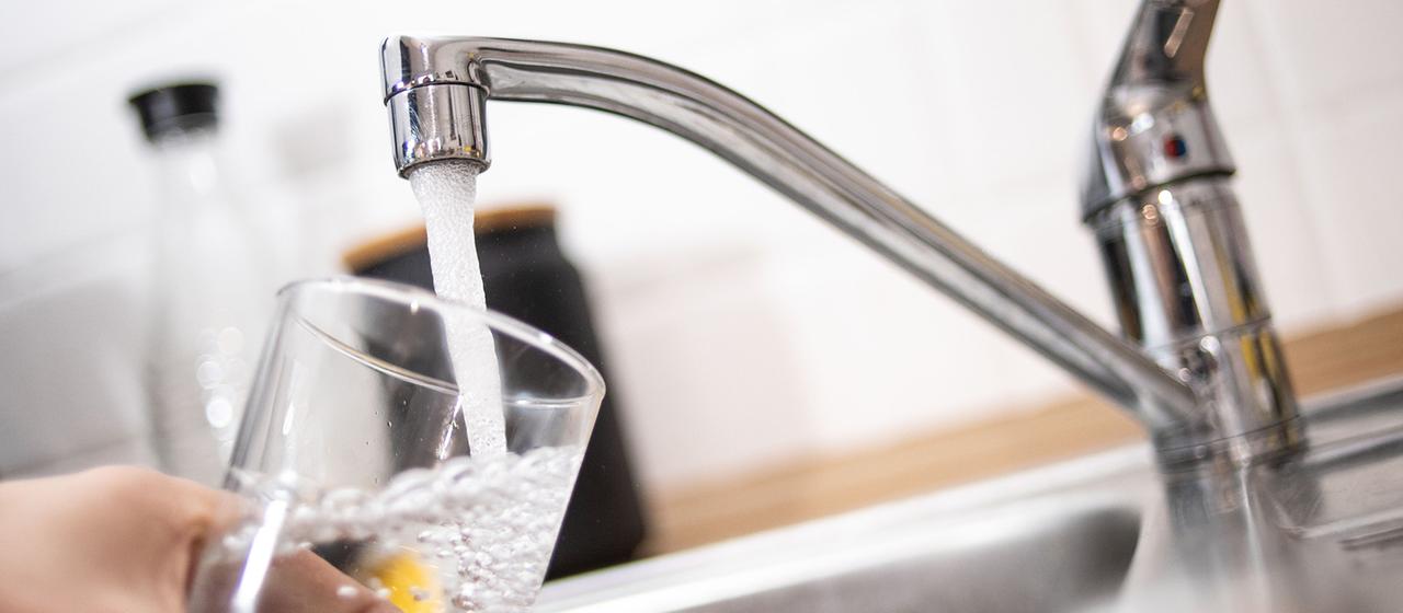 Eine Person hält ein Glas unter einen laufenden Wasserhahn.