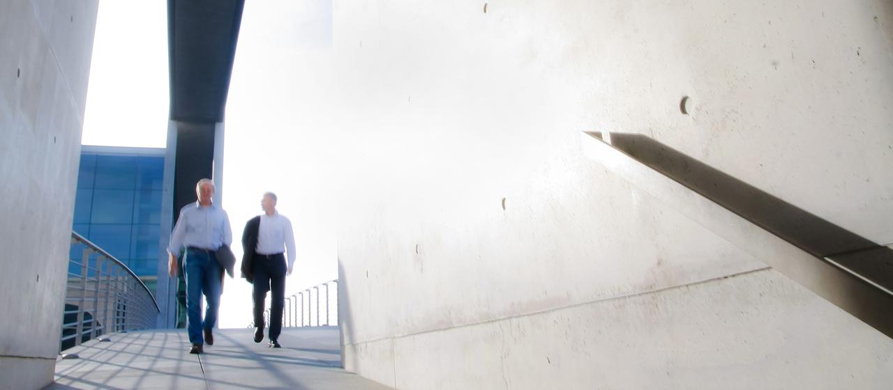Zwei Männer unterhalten sich, während sie einen Gang eines Gebäudes entlanggehen.