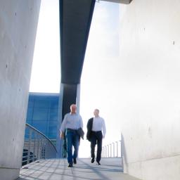 Zwei Männer unterhalten sich, während sie einen Gang eines Gebäudes entlanggehen.