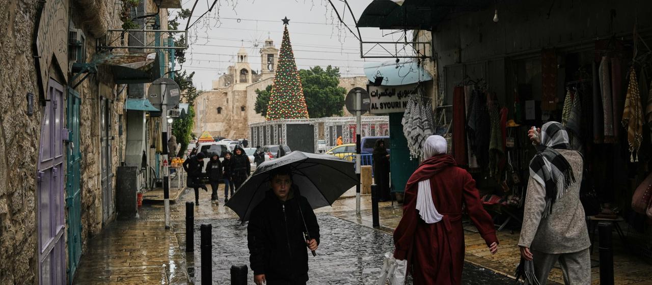 Passanten spazieren durch den Regen auf dem Krippenplatz neben der Geburtskirche in Bethlehem im Westjordanland.