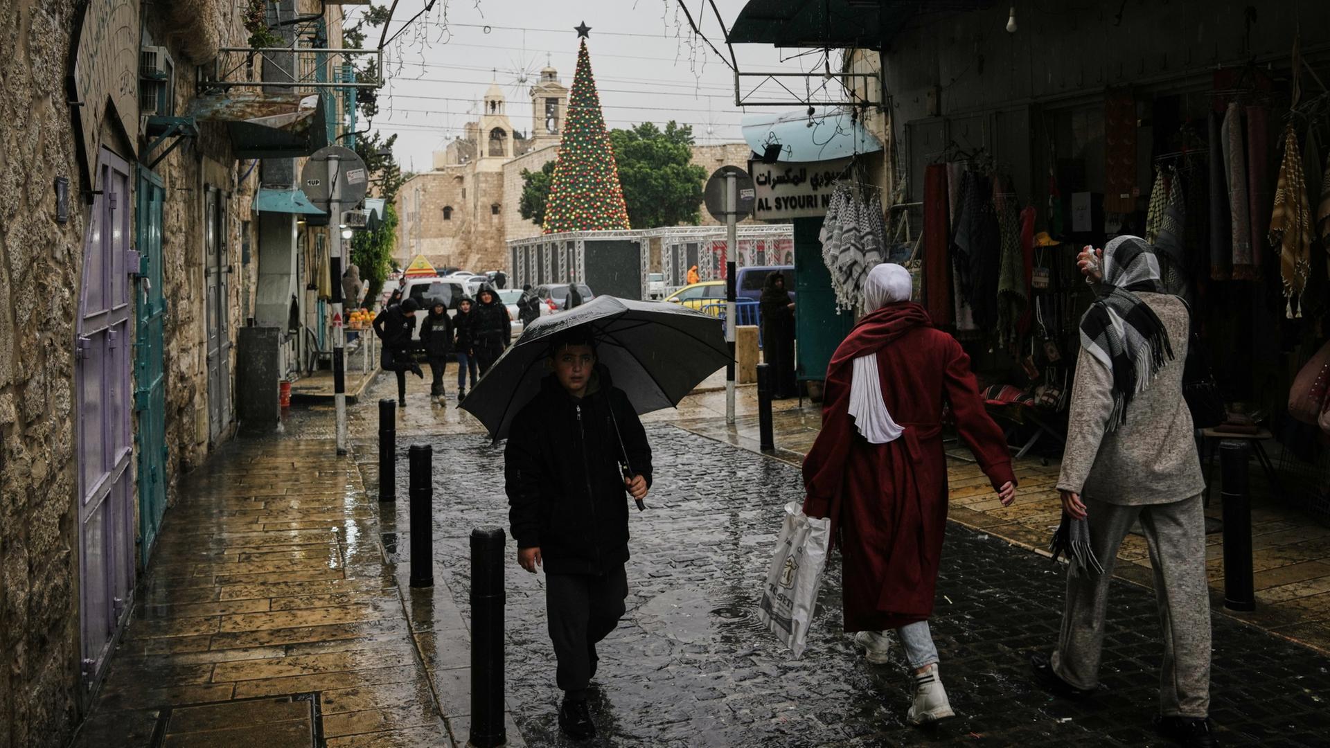 Passanten spazieren durch den Regen auf dem Krippenplatz neben der Geburtskirche in Bethlehem im Westjordanland. | dpa