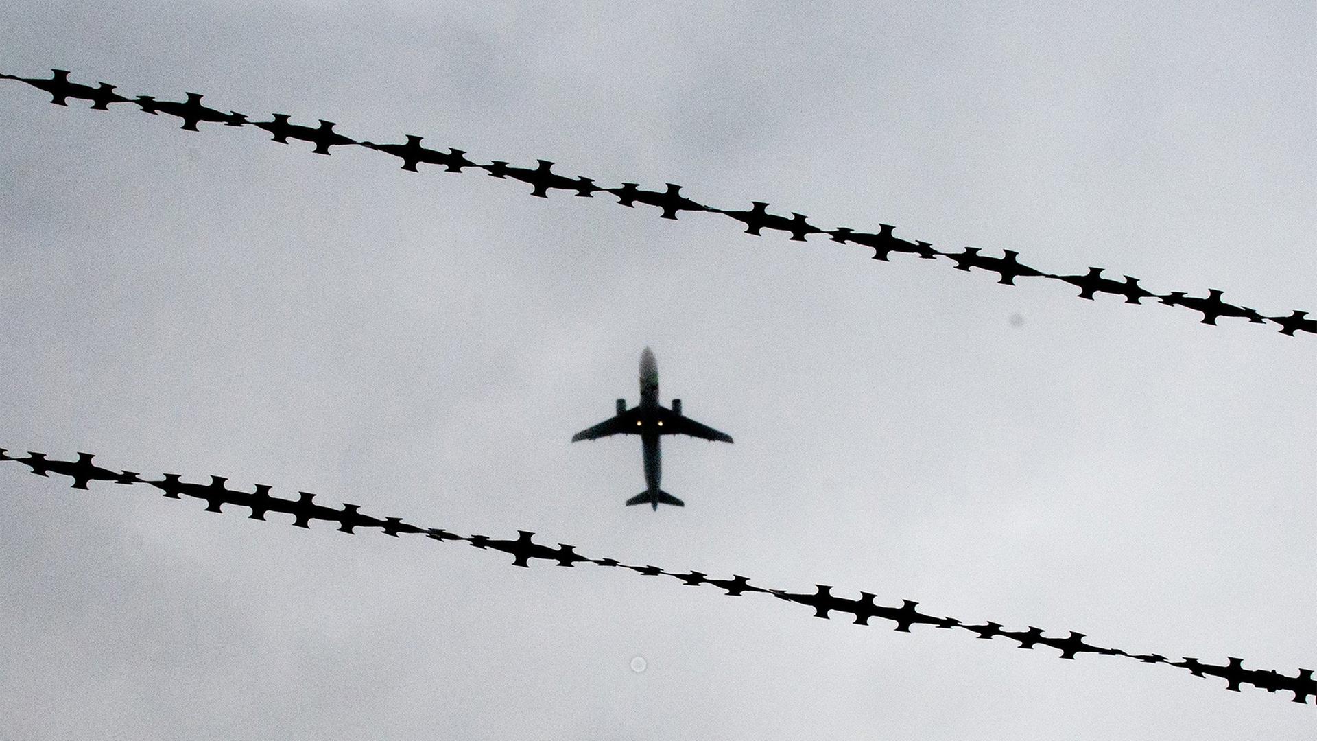 Ein Flugzeug fliegt über einen Stacheldrahtzaun. | dpa