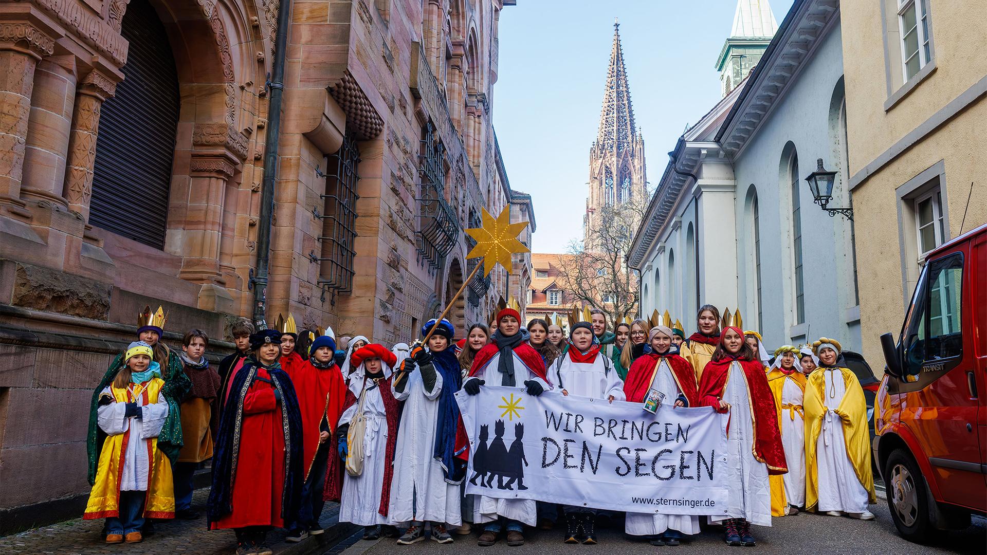 Sternsinger gehen mit einem Banner mit der Aufschrift 
