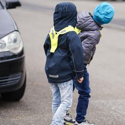 Zwei Kinder stehen hinter einem Auto und schauen auf den Straßenverkehr.