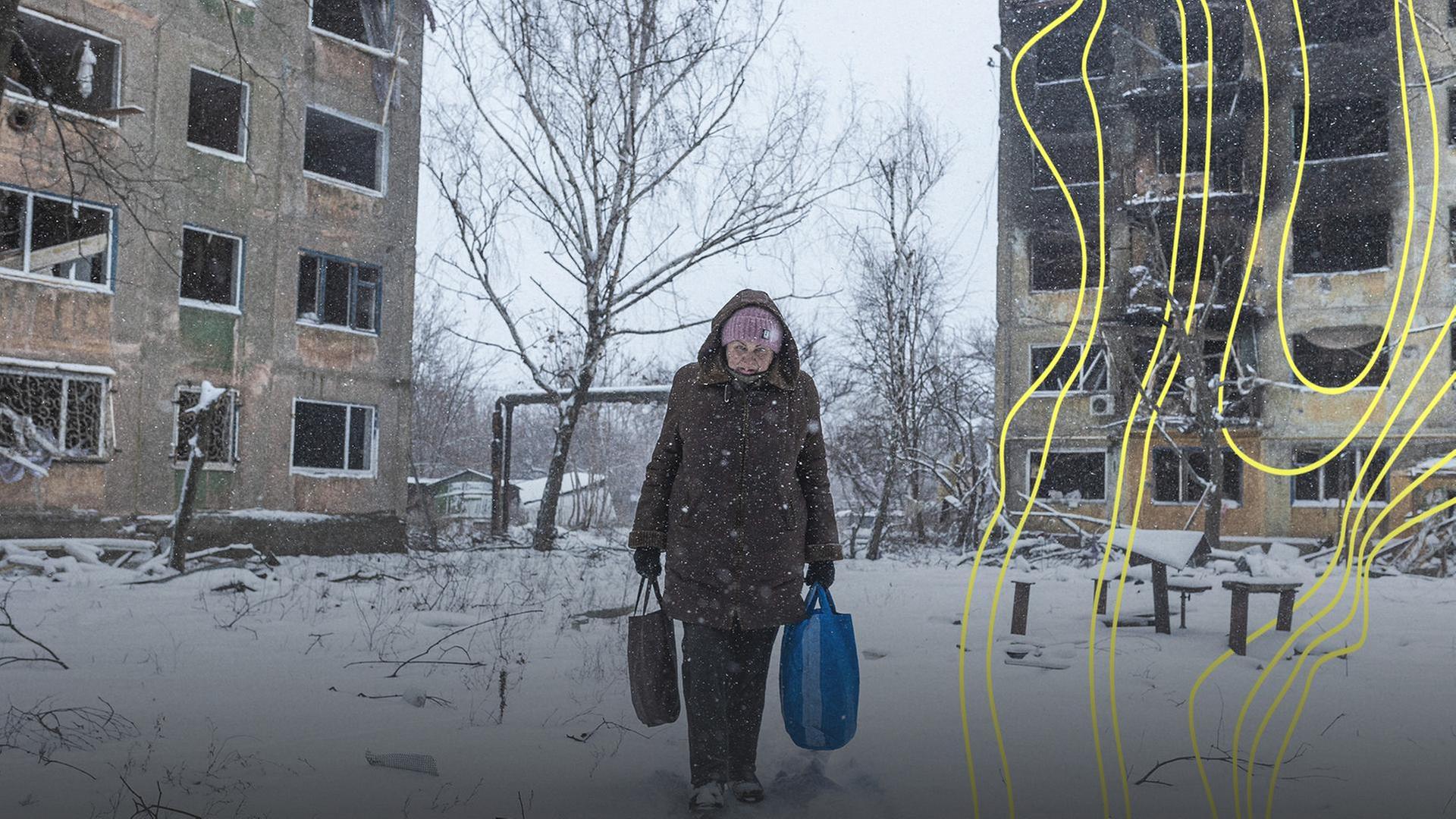 Eine Frau geht mit Taschen in den Händen durch eine durch russische Bomben zerstörte Häuseranlage. | IMAGO/Anadolu Agency