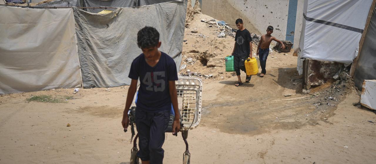 In der Sommerhitze tragen palästinensische Kinder Wasserkanister.