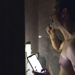 Symbolbild - Stromausfall: A young man brushes his teeth with a toothbrush in a dark bathroom and shines the flashlight in his smartphone. (Quelle: imago images/Bihlmayer)