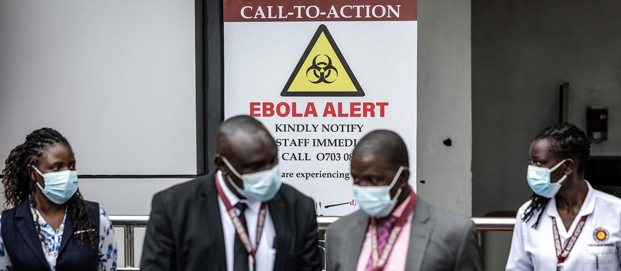 Mitarbeiter eines Krankenhauses vor einem Ebola-Warnschild