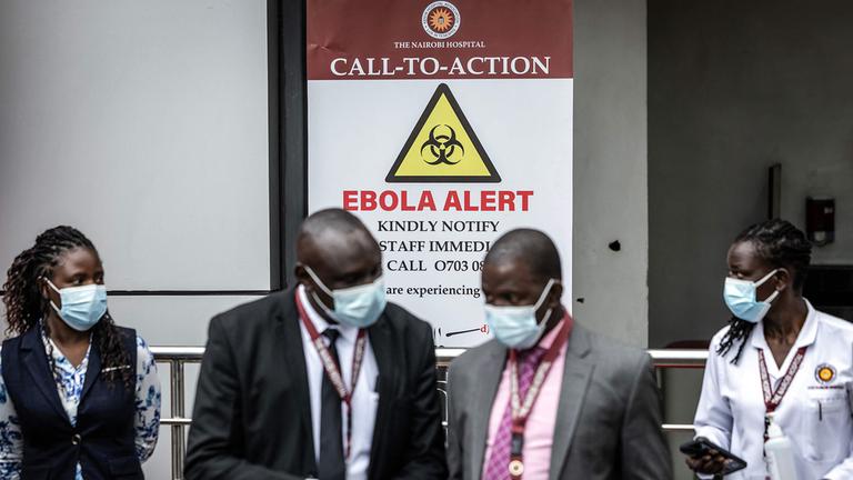 Mitarbeiter eines Krankenhauses vor einem Ebola-Warnschild
