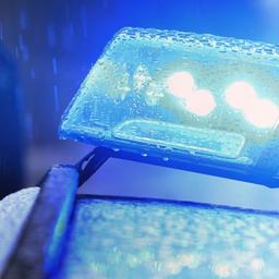 Ein Polizist steht neben einem Streifenwagen mit Blaulicht.