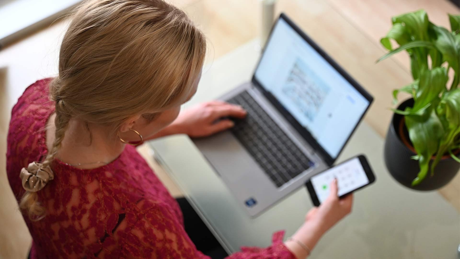 Eine Frau sitzt an einem Tisch und tippt auf einem Laptop, | picture alliance/dpa