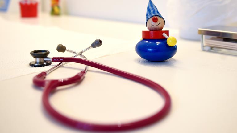 Ein Stethoskop und Kinderspielzeug liegen in einer Kinderarztpraxis auf einem Tisch.
