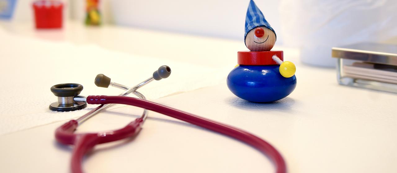 Ein Stethoskop und Kinderspielzeug liegen in einer Kinderarztpraxis auf einem Tisch.