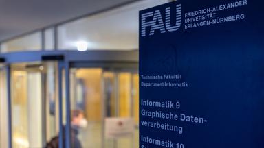 Ein junger Mann betritt den Eingangsbereich des Bereichs Informatik der Friedrich-Alexander-Universität Erlangen-Nürnberg.