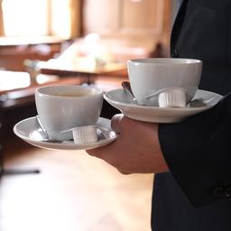 In einem Restaurant bringt ein Kellner zwei Tassen Kaffee an einen Tisch.