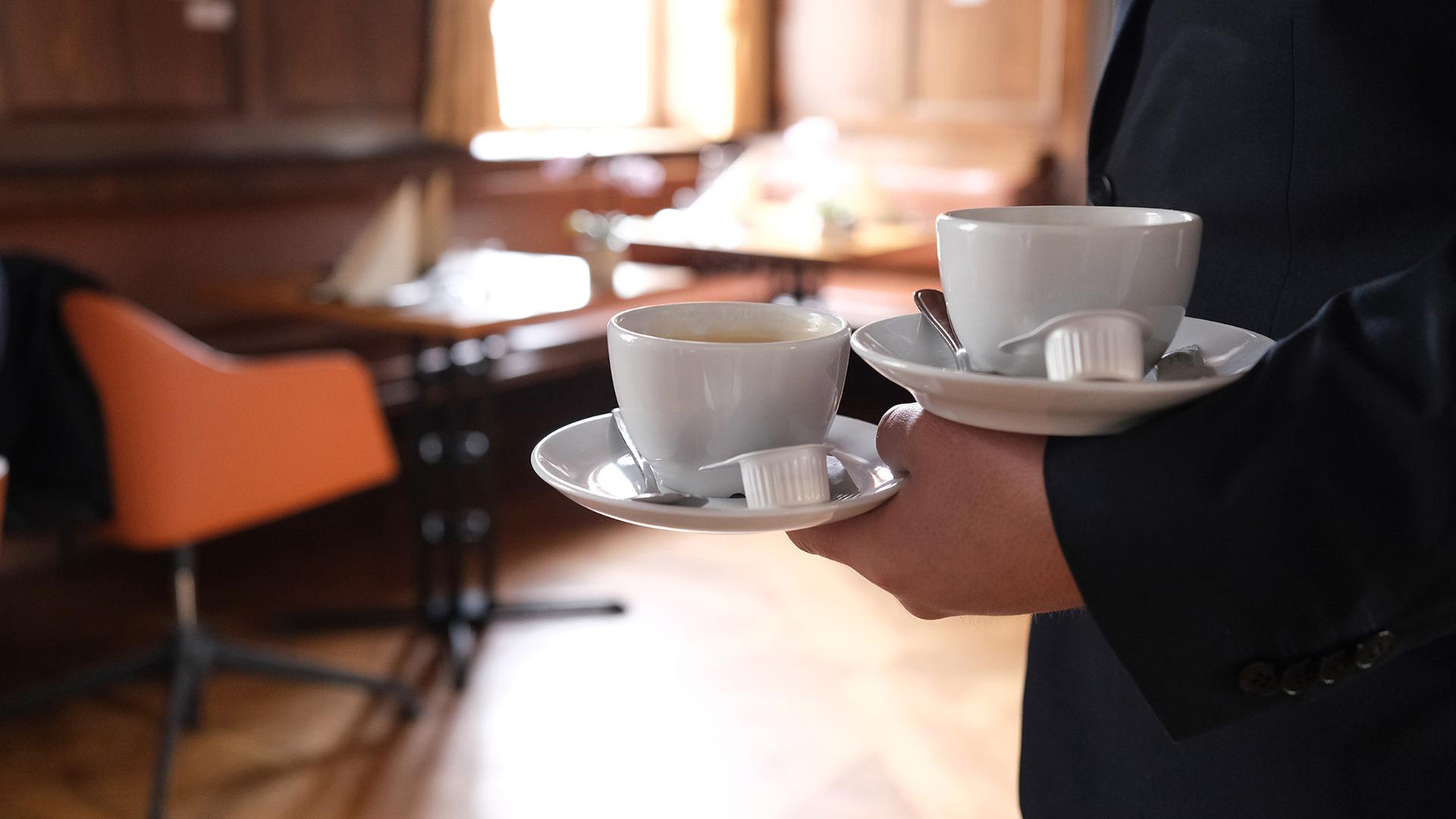 In einem Restaurant bringt ein Kellner zwei Tassen Kaffee an einen Tisch. | dpa