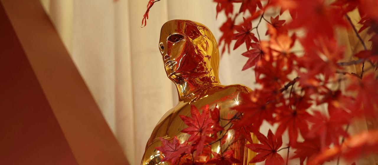 Eine Oscar Statue wird teilweise verdeckt von roten Blättern.