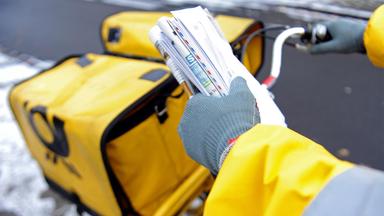 Postbote hält Briefe und Zeitungen in der Hand.