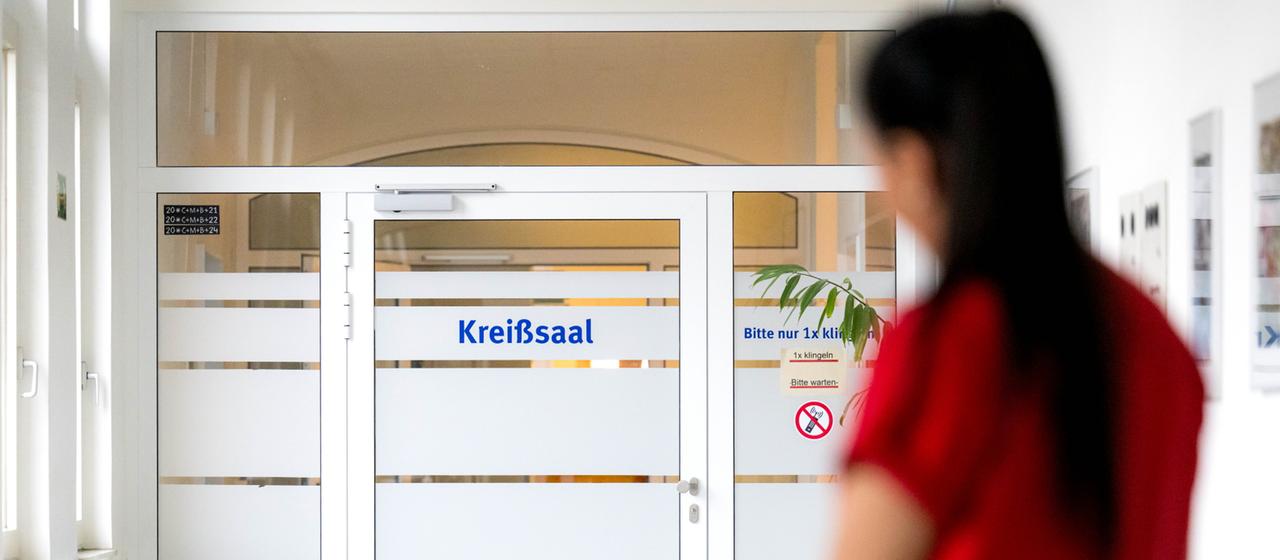 Eine Hebamme schiebt ein Säuglingsbett zum Kreißsaal.