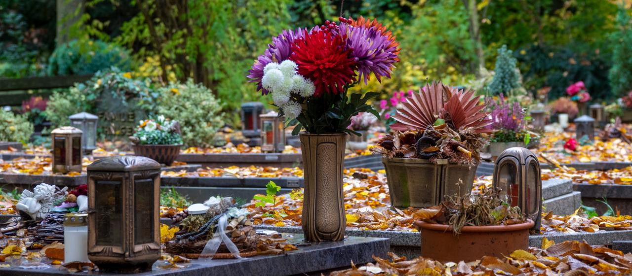 Herbstlaub liegt auf Gräbern auf einem Friedhof.
