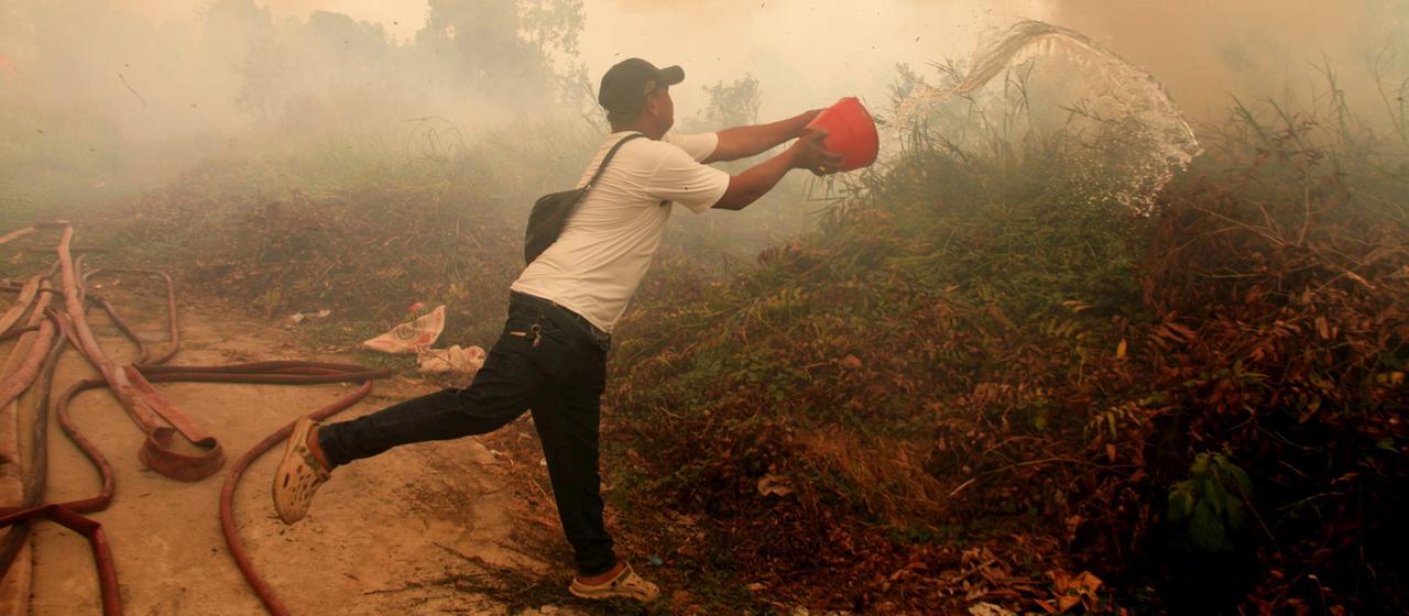 Ein Mann bekämpft einen Vegetationsbrand in Indonesien mit einem Eimer Wasser.
