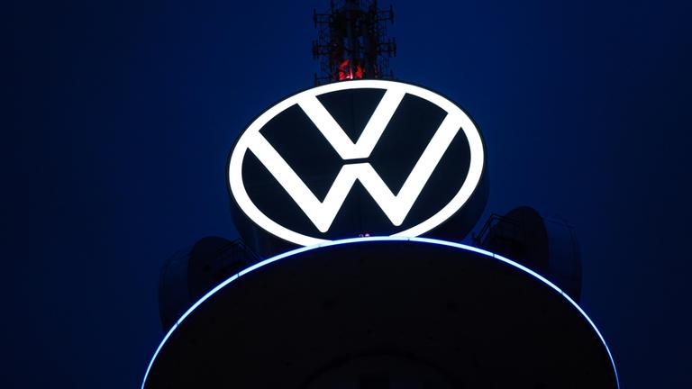 Das Volkswagen-Logo leuchtet auf dem VW-Tower in Hannover vor dunklem Himmel.