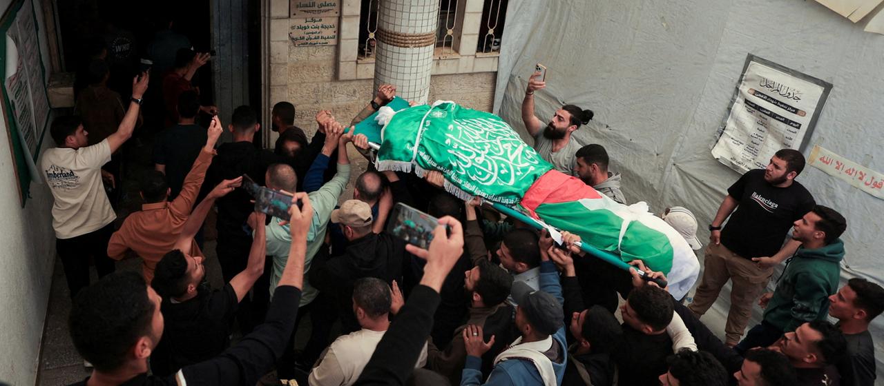 Menschen tragen eine Bahre, die mit einer Flagge der Terrororganisation Hamas bedeckt ist.