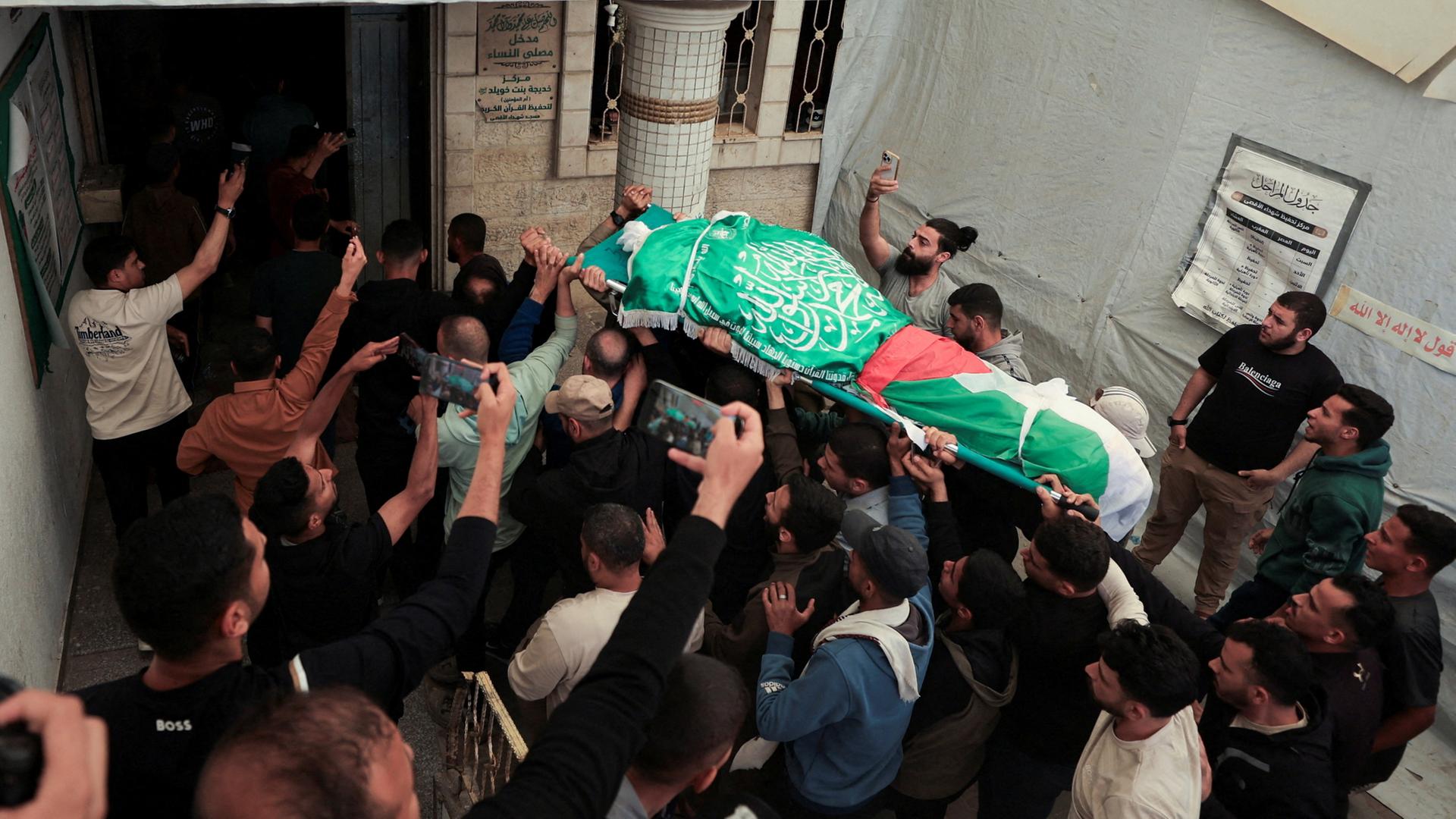 Menschen tragen eine Bahre, die mit einer Flagge der Terrororganisation Hamas bedeckt ist. | REUTERS